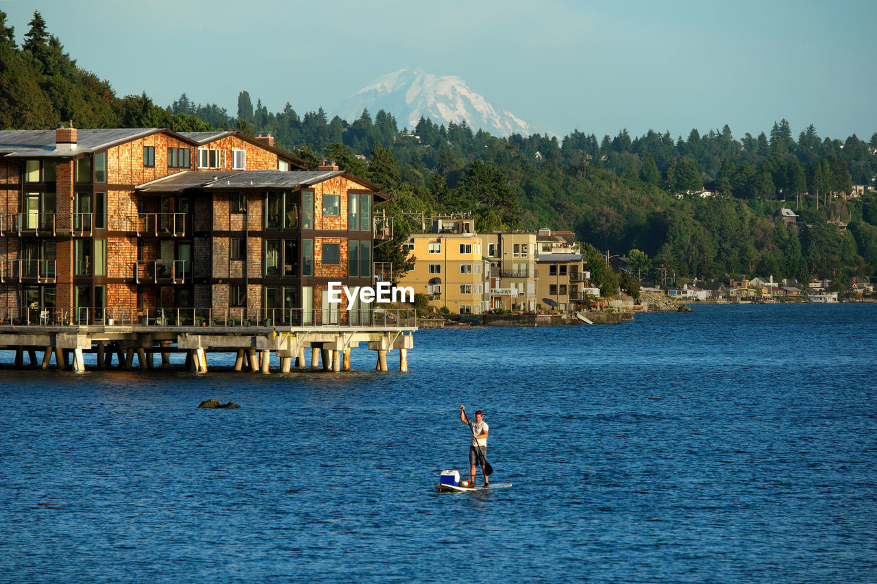 Man paddleboarding on lake with buildings in background