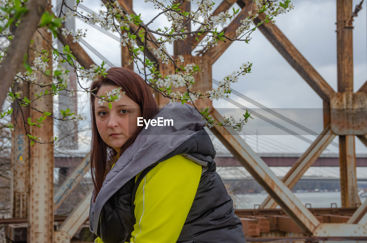 PORTRAIT OF YOUNG WOMAN STANDING AGAINST TREE