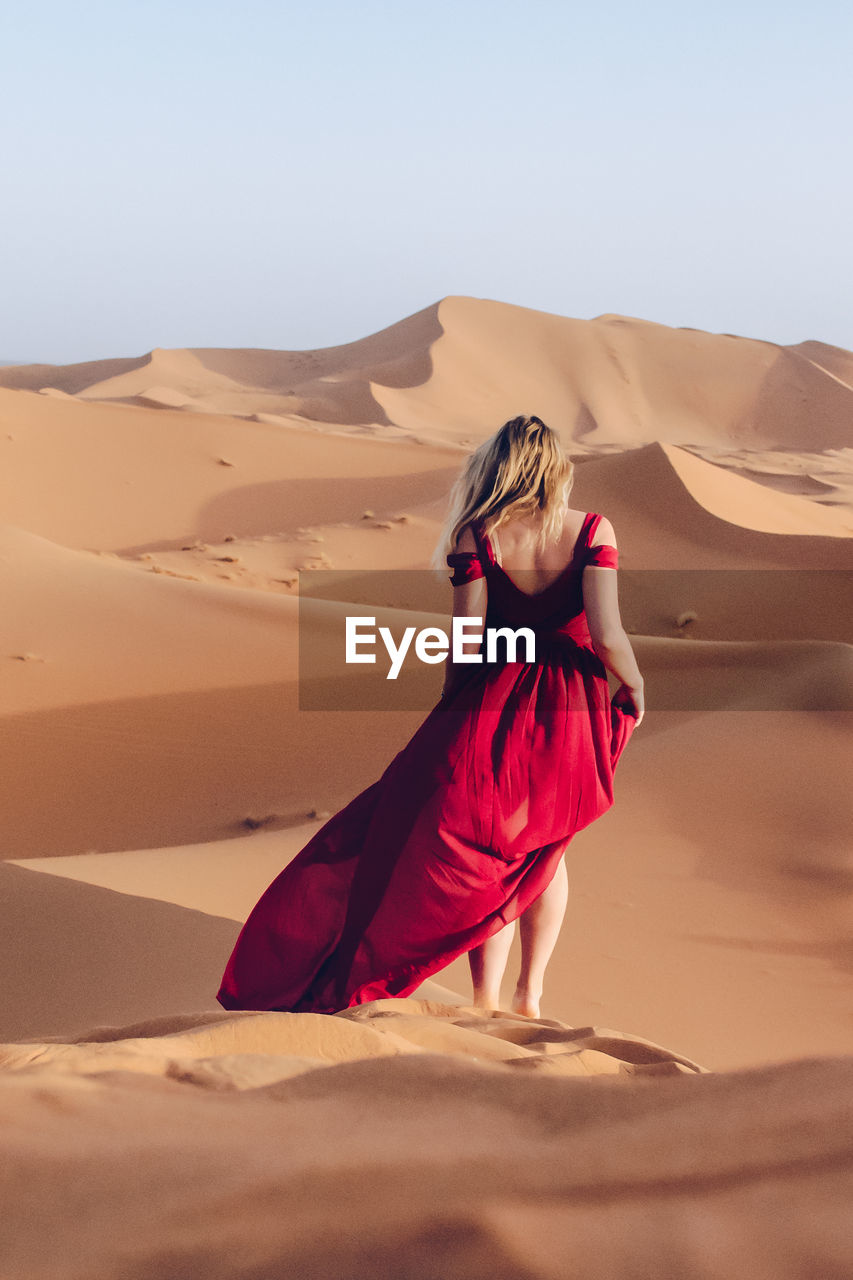 Rear view of woman standing in desert against clear sky