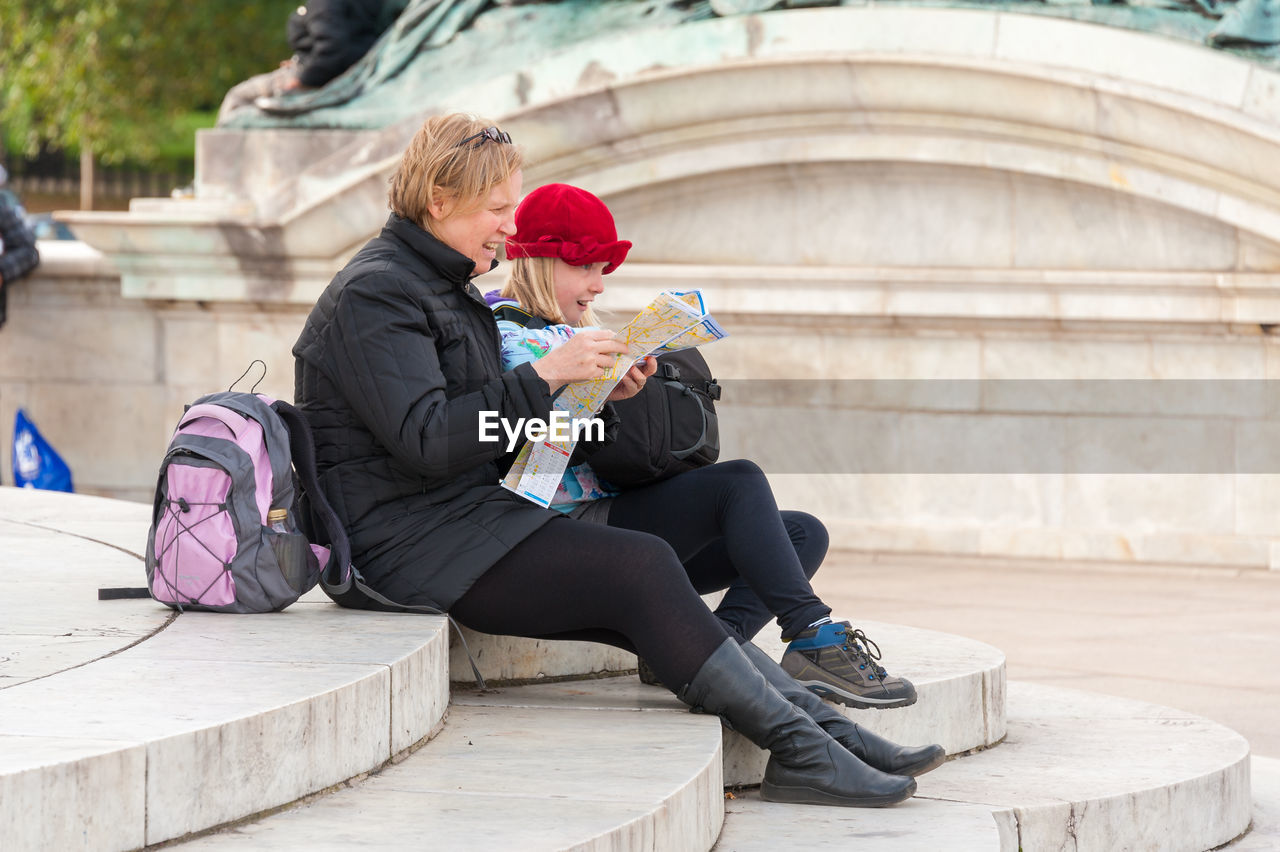 Mother reading map while sitting with daughter on steps