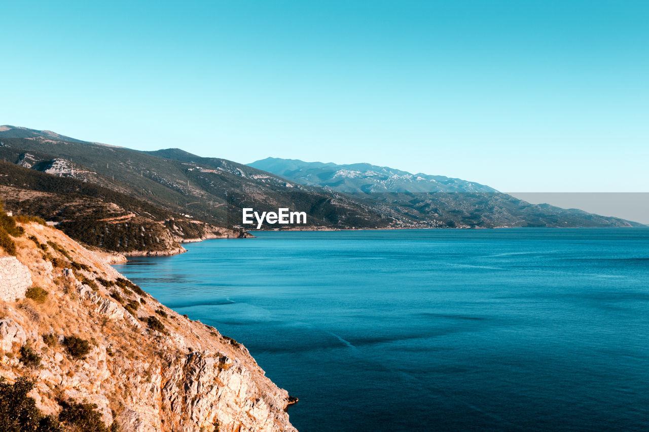 Scenic view of sea and mountains against clear blue sky