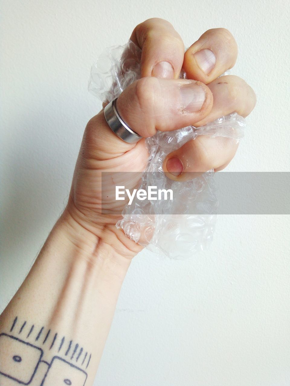 Cropped hand of man crumpling bubble wrap against white wall