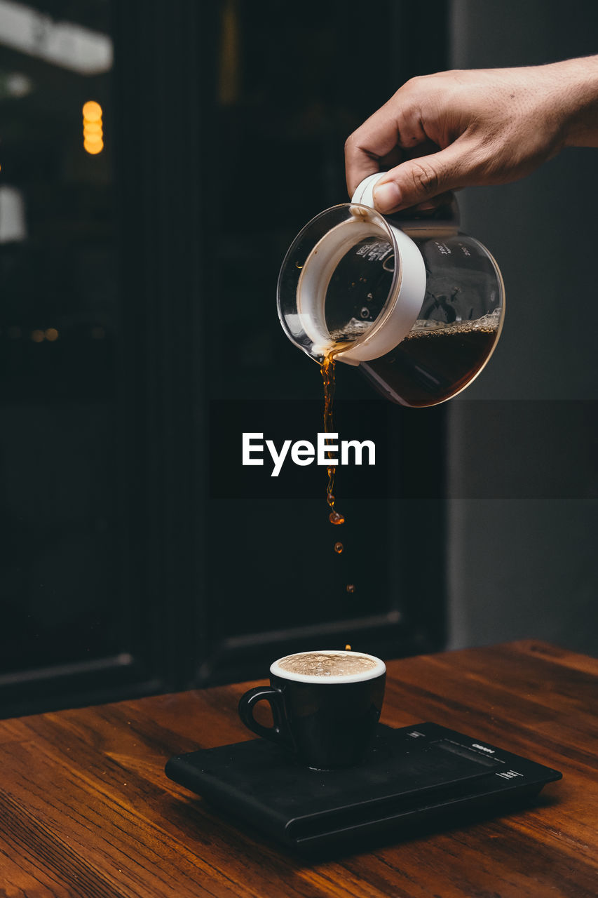 Cropped hand of person pouring coffee in cup on table