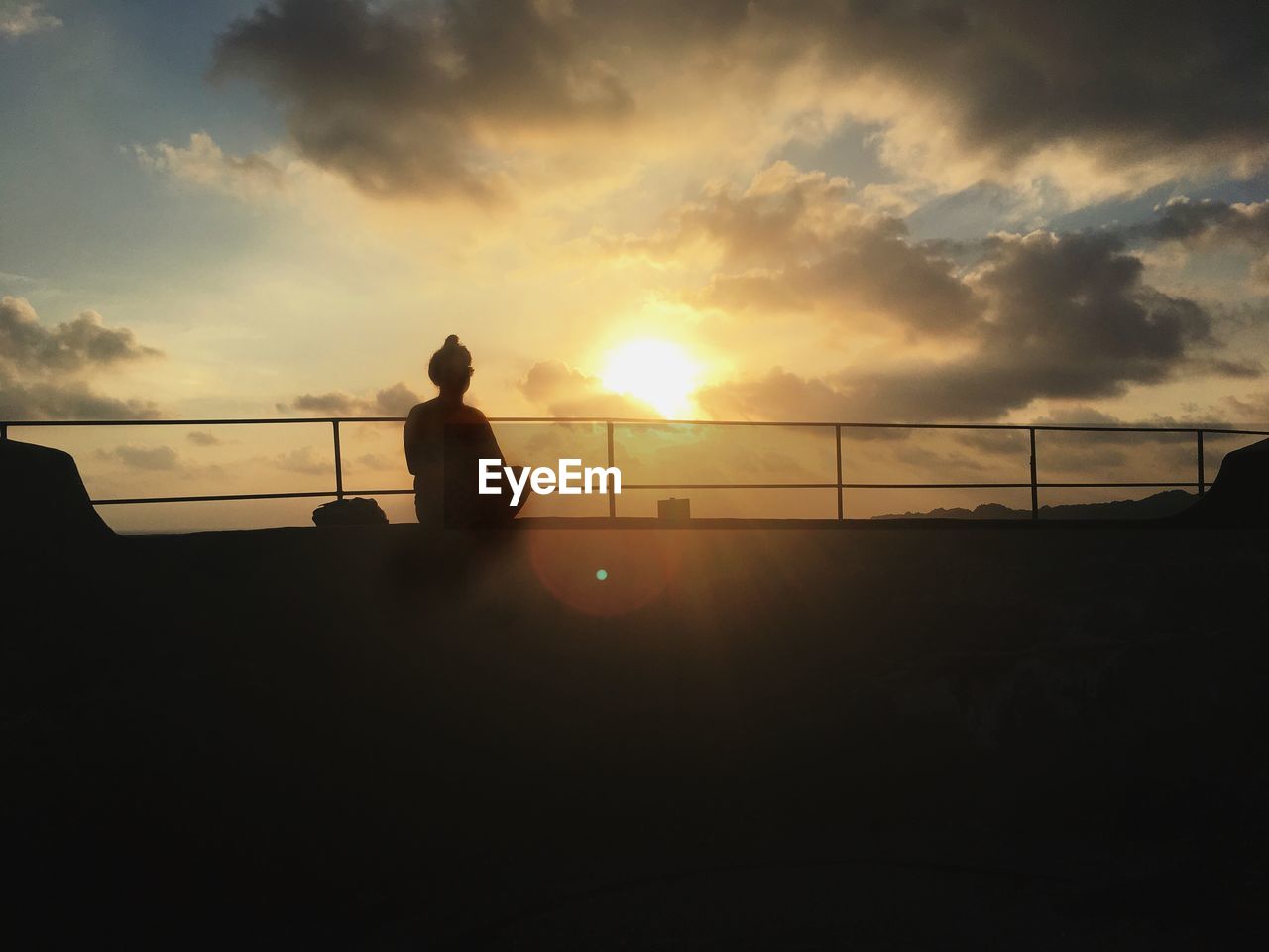 SILHOUETTE MAN STANDING BY RAILING AGAINST ORANGE SKY