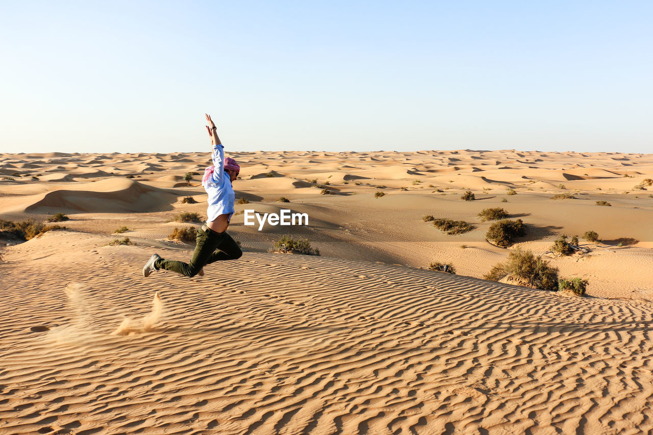 Full length side view of mid adult man jumping in desert