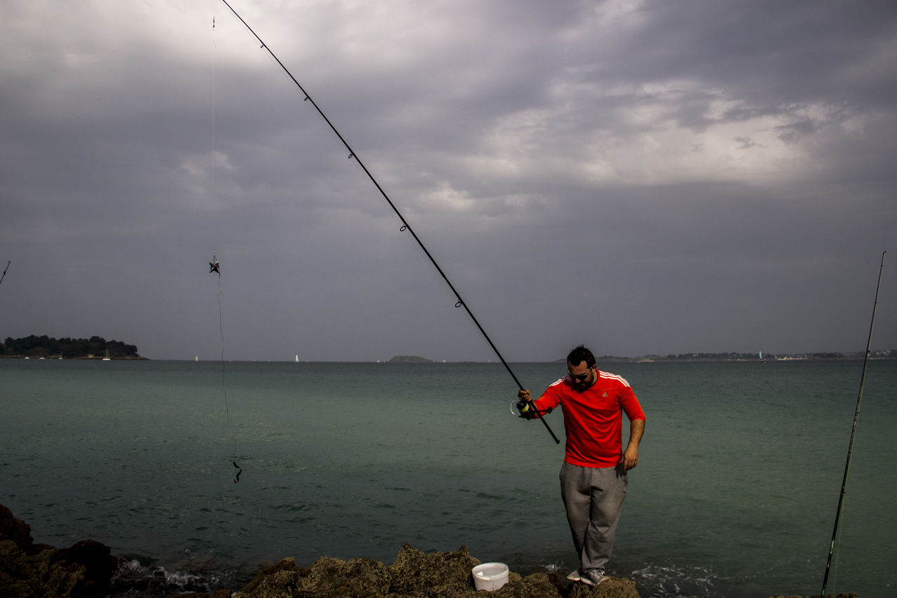 water, sky, fishing, fishing rod, cloud, rod, sea, one person, recreation, activity, nature, angling, casting, full length, men, leisure activity, beach, beauty in nature, adult, standing, land, holiday, scenics - nature, lifestyles, fishing industry, vacation, outdoors, trip, fisherman, sports, rock, overcast, motion, holding, rear view, day, coast, nautical vessel, tranquil scene, environment