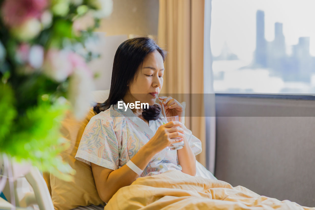 Woman patient drinking water while sitting on the bed in hospita