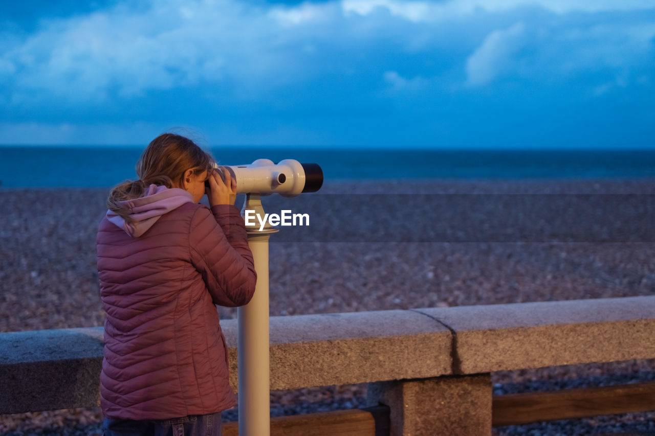 rear view of woman photographing sea against cloudy sky