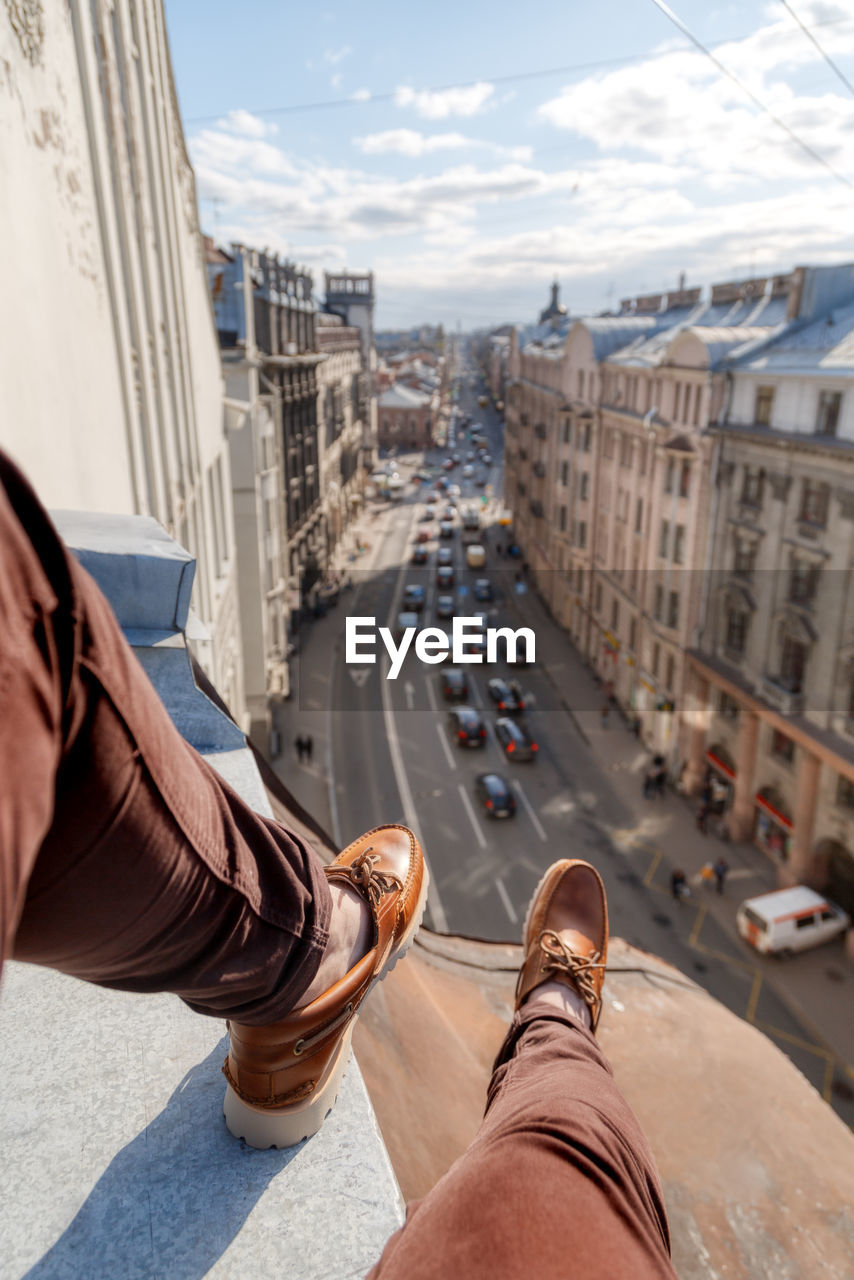 Man legs in burgundy trousers and brown loafers. male sitting on edge of roof in saint petersburg