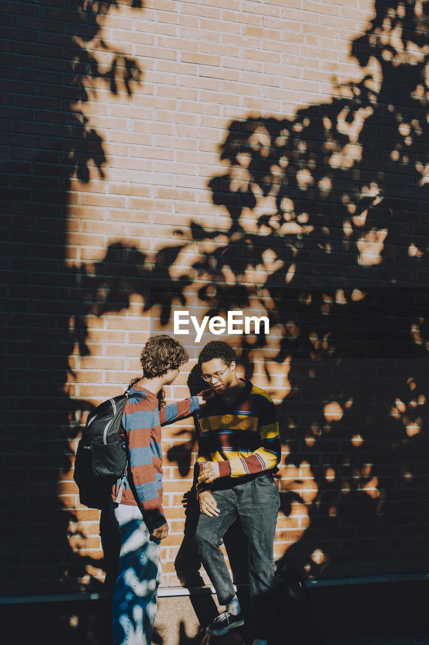 Teenager consoling friend while standing against brick wall