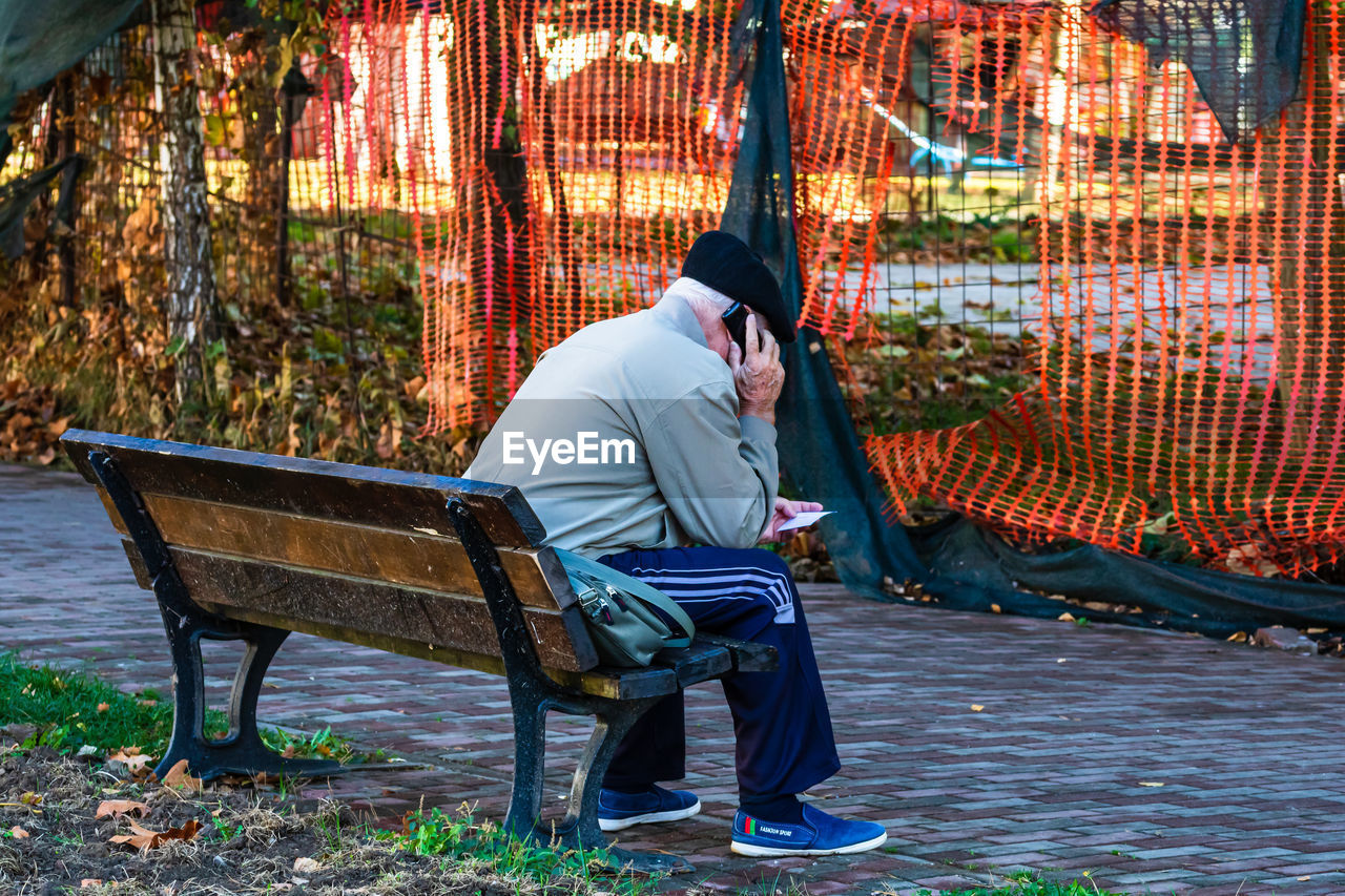 REAR VIEW OF MAN SITTING ON BENCH IN PARK