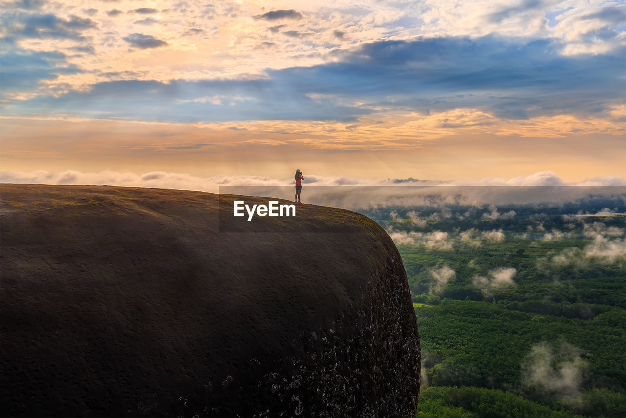 Mid distance of woman standing on mountain against cloudy sky during sunset