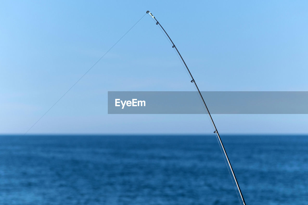 FISHING ROD OVER SEA AGAINST CLEAR SKY