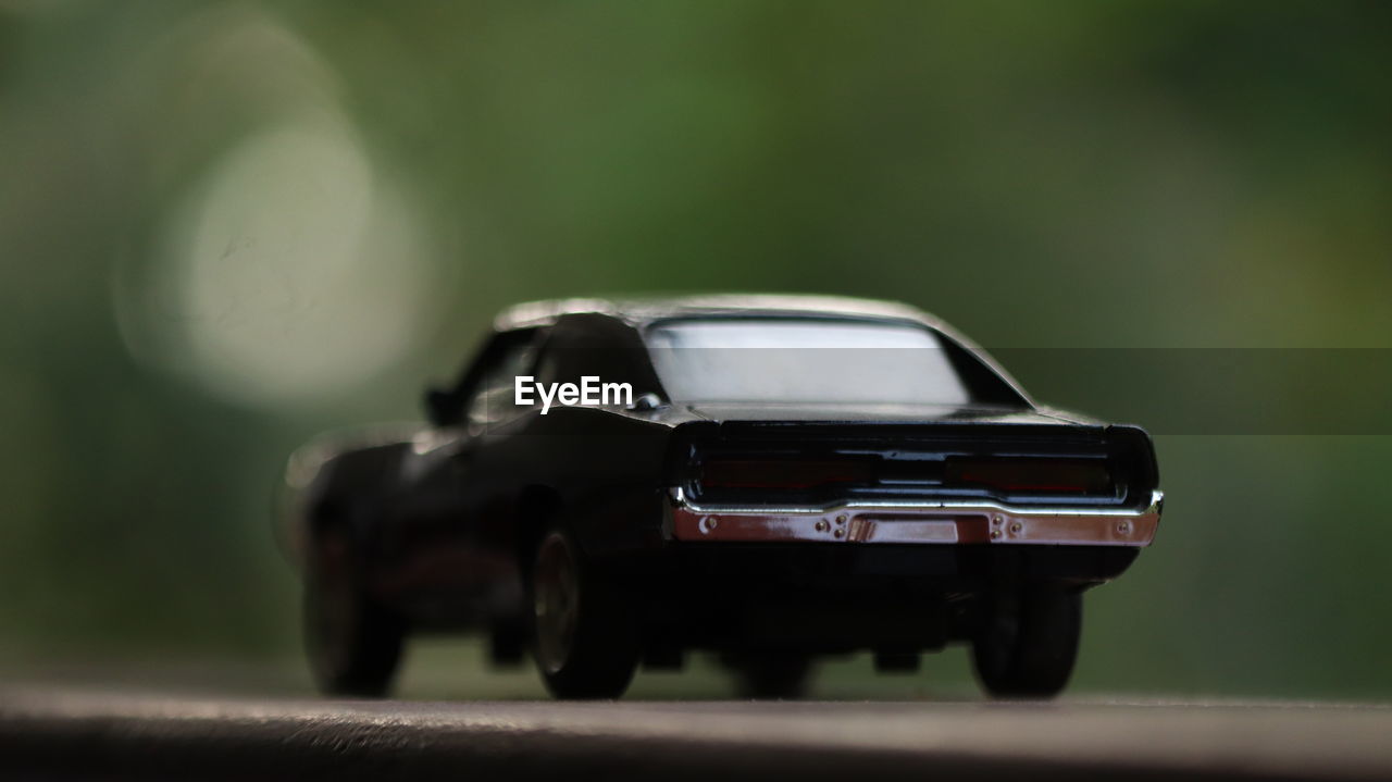 A black die cast toy car on a greenery background.