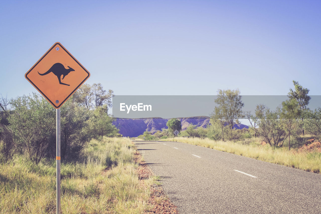 Kangaroo crossing sign by road against sky