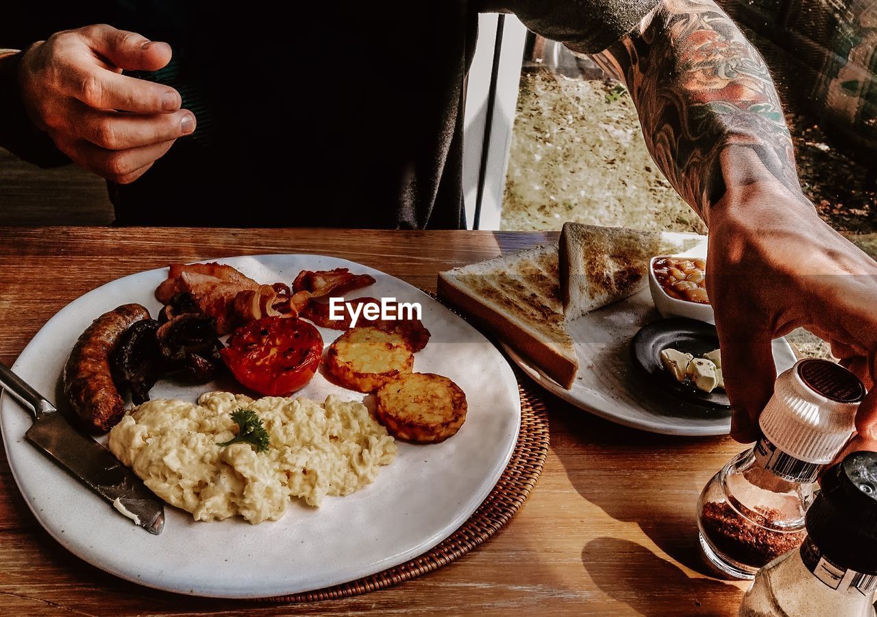 Close-up of tattooed man enjoying traditional english breakfast