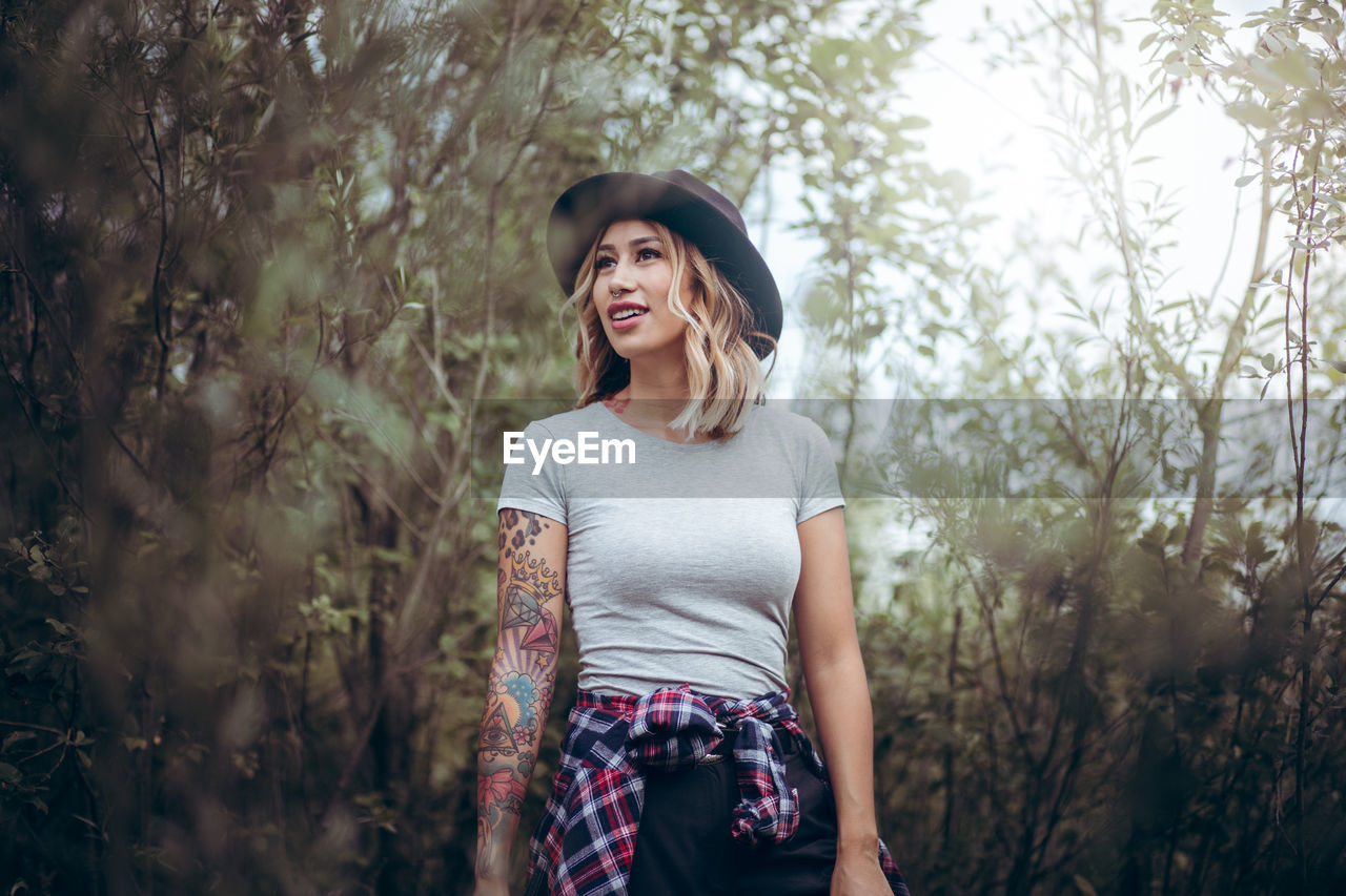 Young woman wearing hat while standing in forest