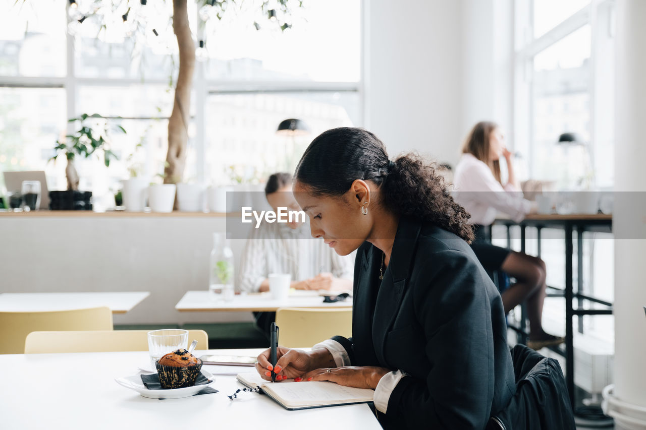 Businesswoman writing in diary while having muffin at office cafeteria