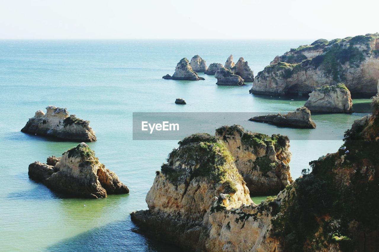 Scenic view of cliff by sea against clear sky