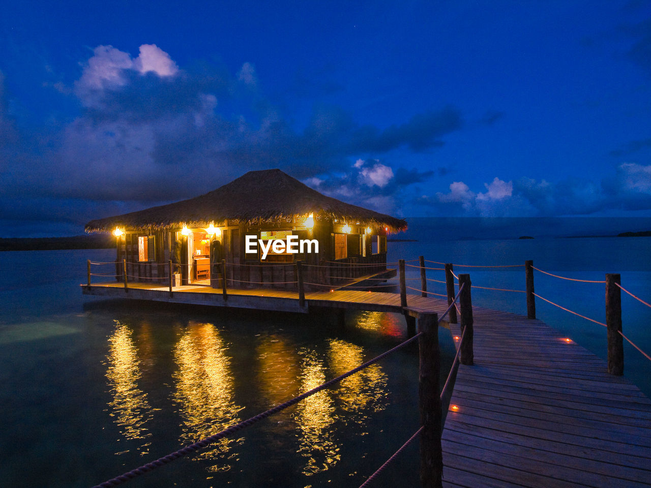 ILLUMINATED BUILDING BY SEA AGAINST SKY AT DUSK