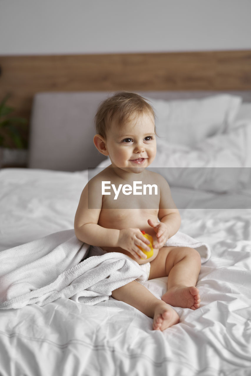 Cute baby boy sitting on bed at home