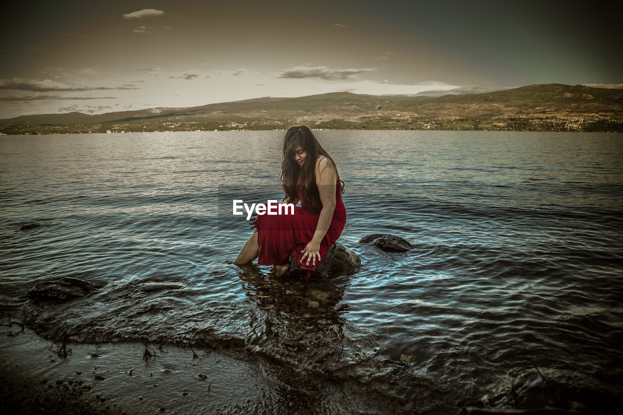 WOMAN STANDING IN LAKE AGAINST MOUNTAIN