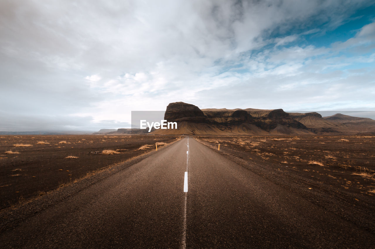 Empty road by mountains against sky