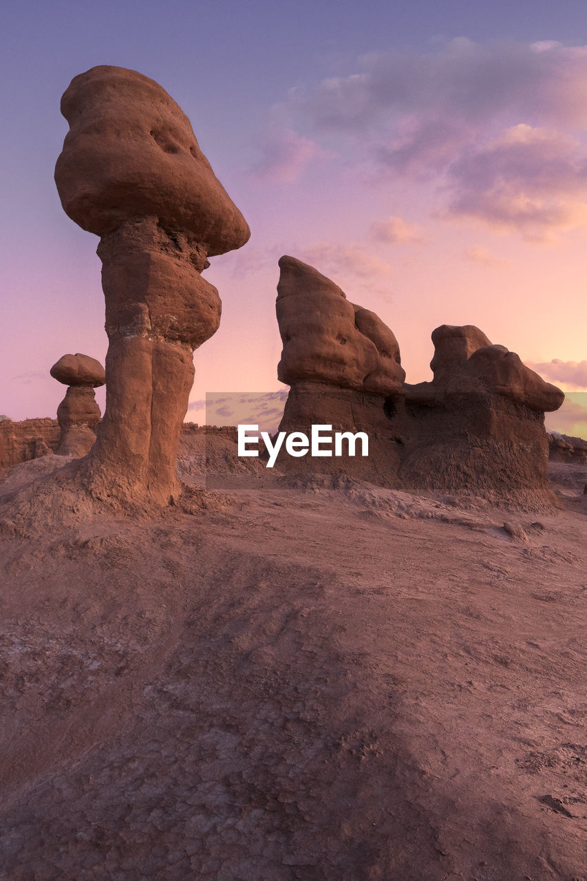 Mushroom shaped rock pinnacles located near hole in dry ground against cloudy sundown sky in goblin valley state park in evening in utah, usa