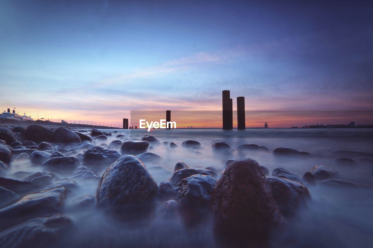 Rocks in sea against sky during sunset