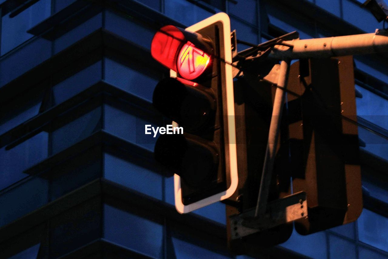 LOW ANGLE VIEW OF ROAD SIGNAL AGAINST ILLUMINATED BUILDING