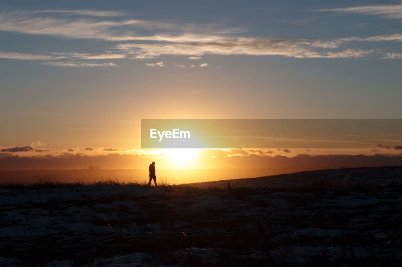 Silhouette man standing on land against sky during sunset