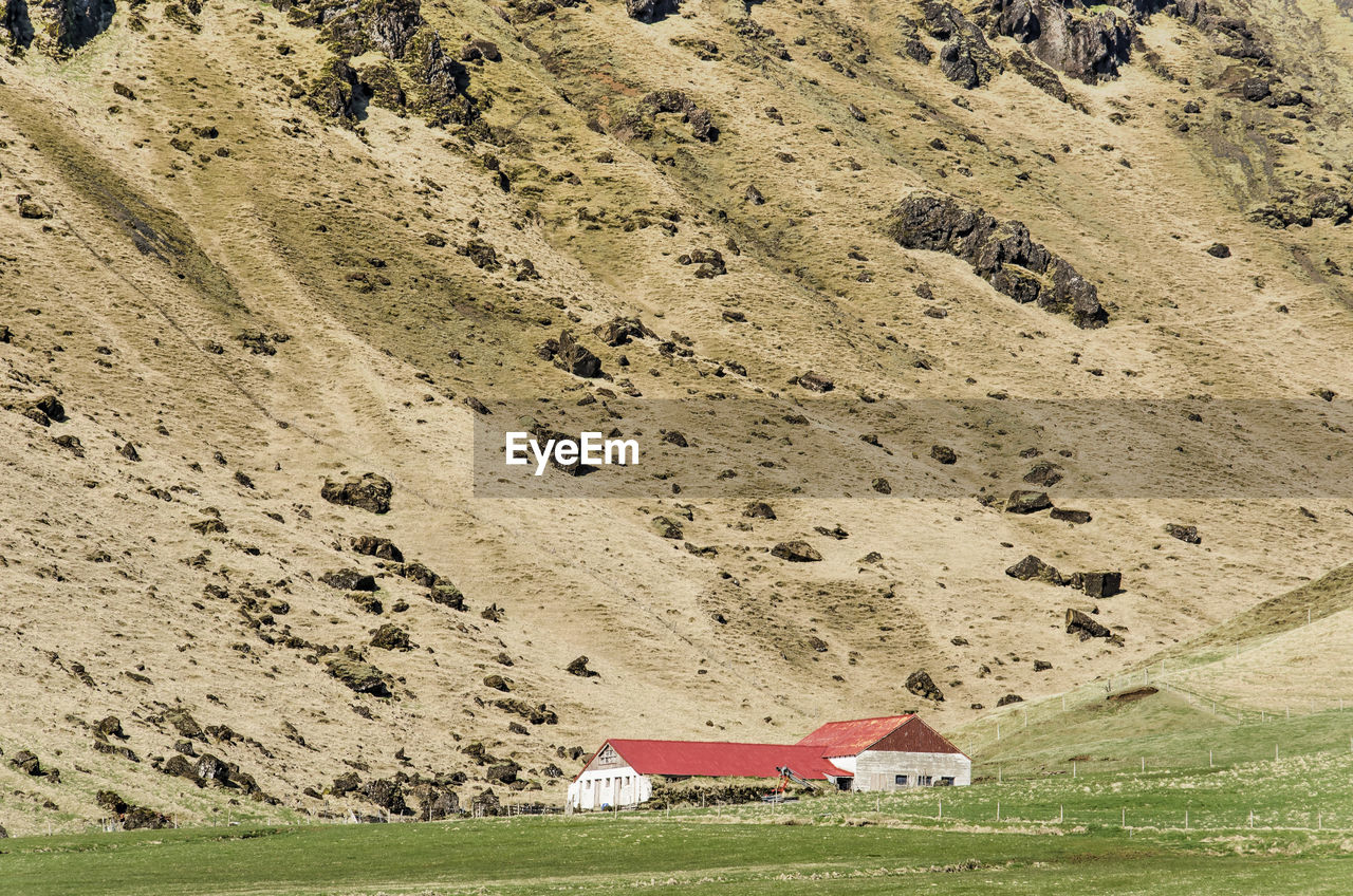 Small barns at the foot of a steep mountain slope with scattered rocks
