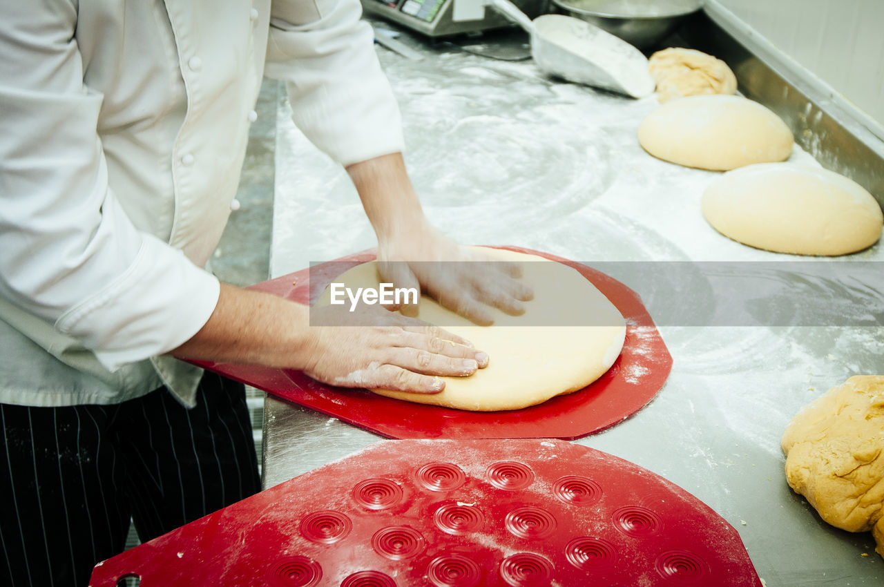 Midsection of chef kneading dough on table in commercial kitchen