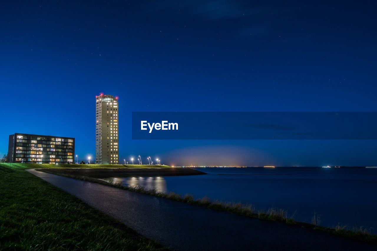 VIEW OF ILLUMINATED CITYSCAPE AGAINST BLUE SKY