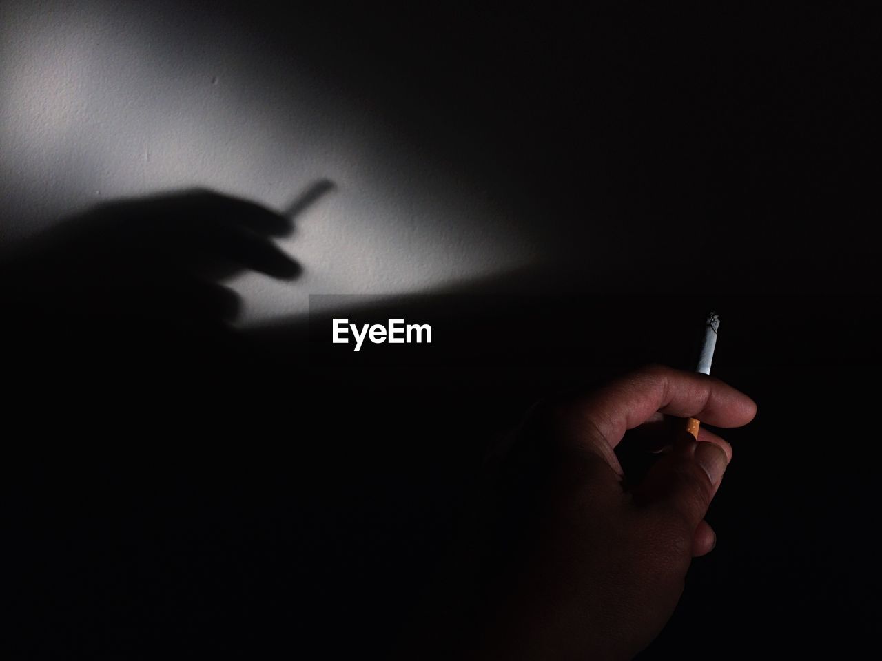 Cropped hand holding cigarette with shadow on wall
