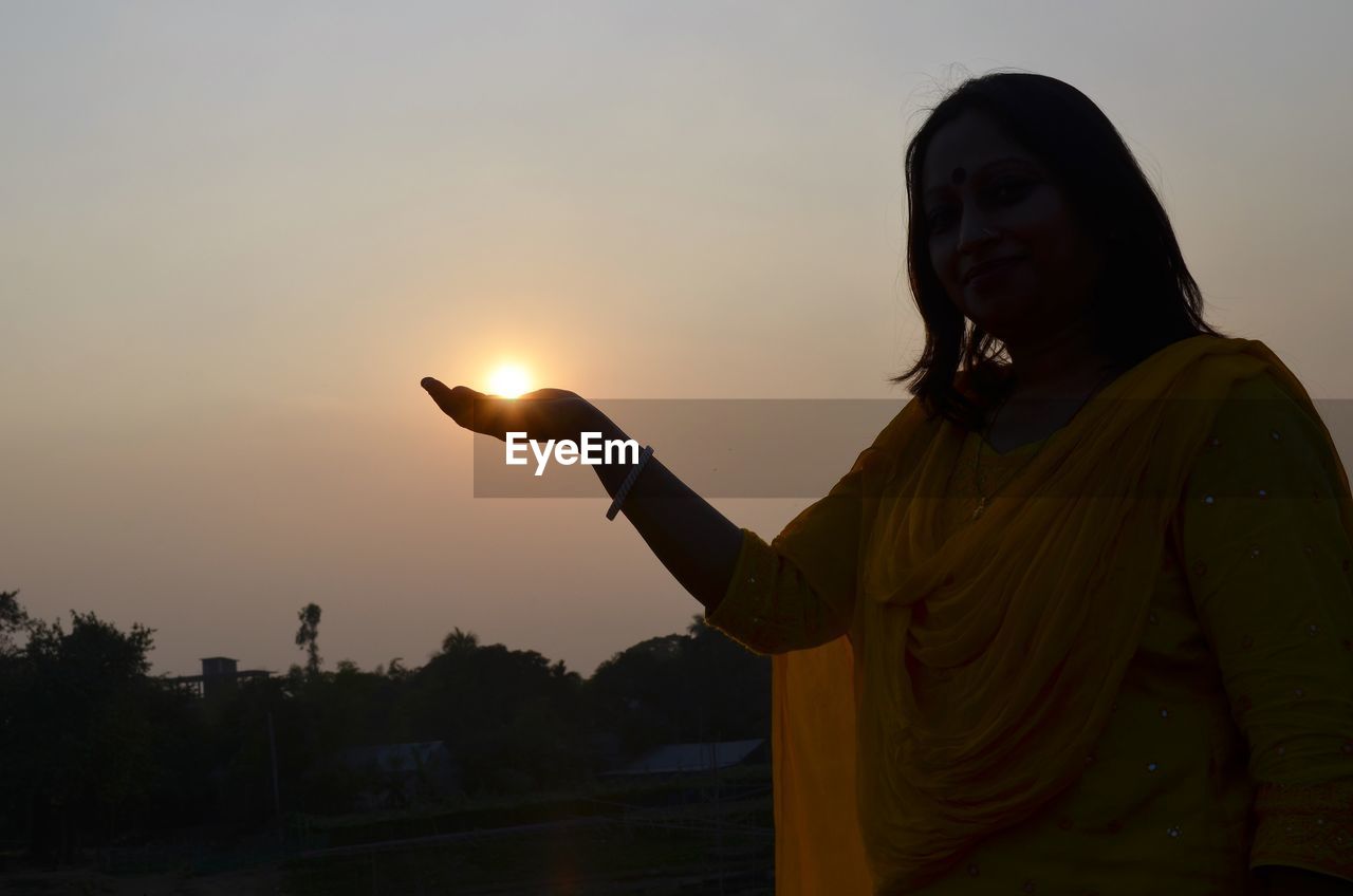 Optical illusion of woman holding sun against sky during sunset