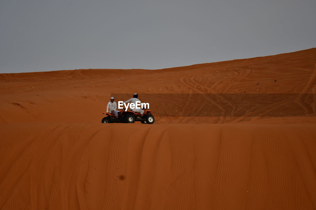 MAN RIDING MOTORCYCLE ON SAND DUNE