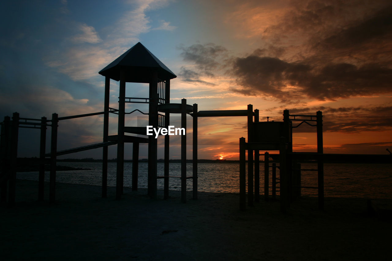 Silhouette built structure on beach against sky during sunset