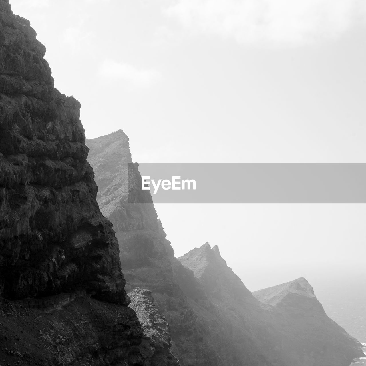 rock, mountain, sky, black and white, scenics - nature, beauty in nature, environment, nature, landscape, land, rock formation, monochrome photography, travel, cliff, cloud, monochrome, travel destinations, fog, mountain range, no people, non-urban scene, tranquility, terrain, outdoors, tranquil scene, day, tourism, geology, water, coast, mountain peak, sea, physical geography, trip, holiday