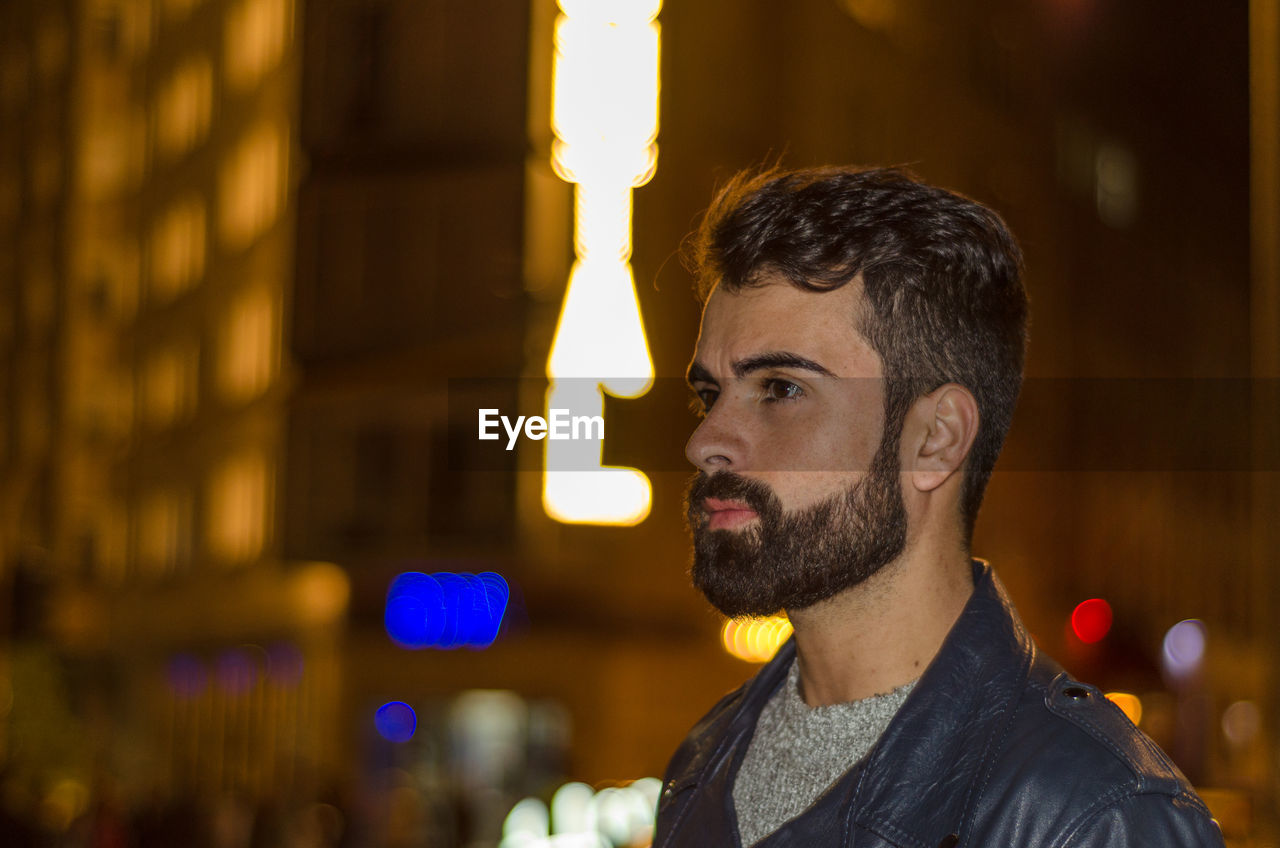 Young man looking away in city at night