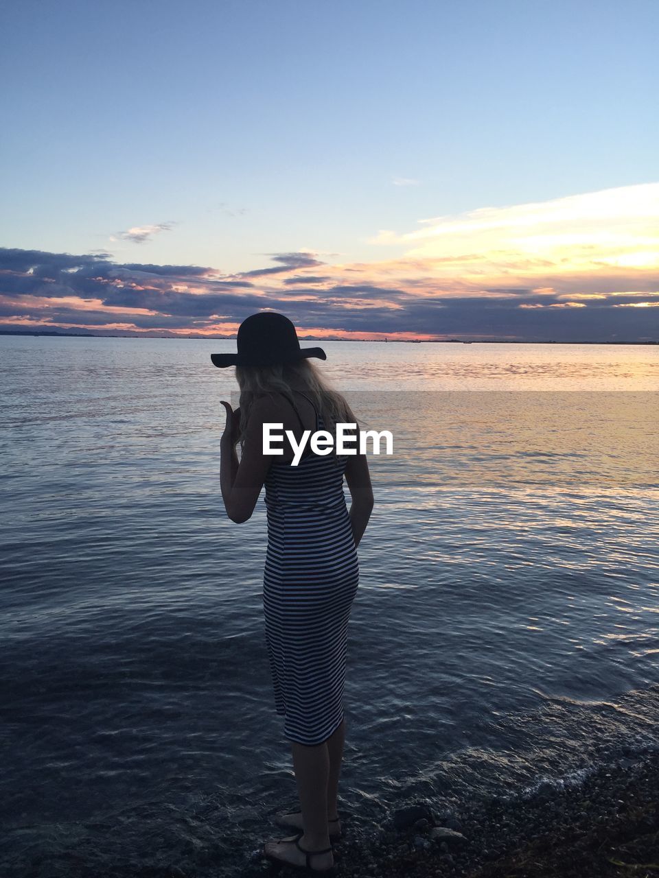 Rear view of teenage girl standing by sea against sky during sunset