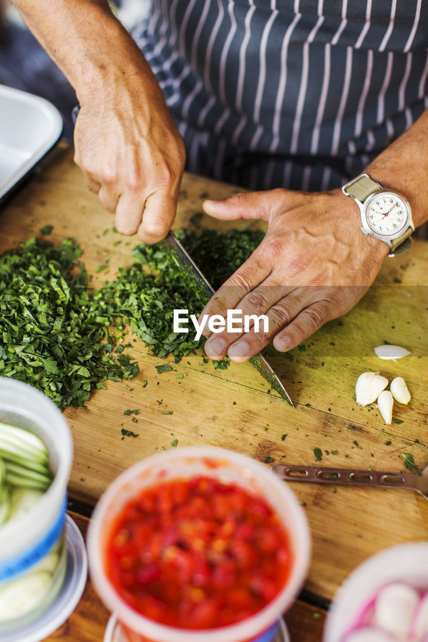 A man's hands cutting cilantro on a wooden cutting board