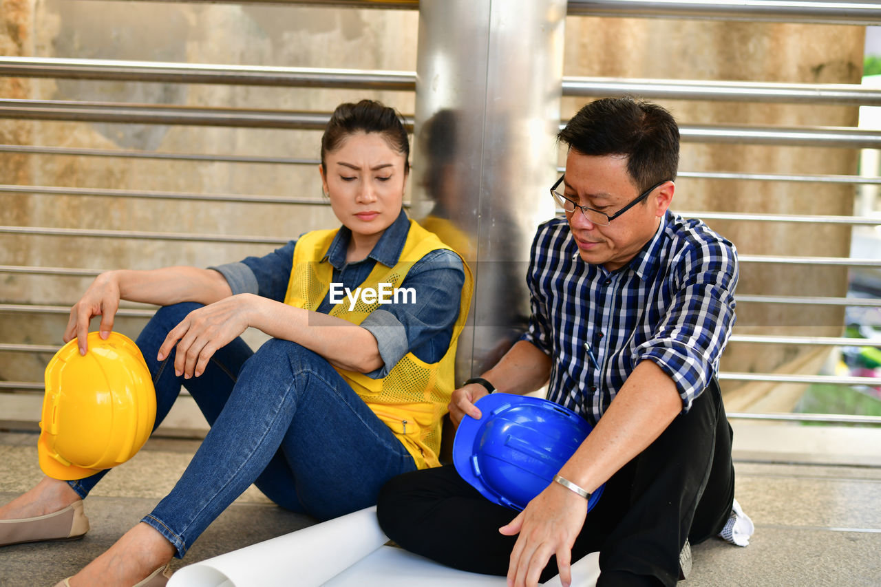 Worried engineers working over blueprint while sitting on covered bridge