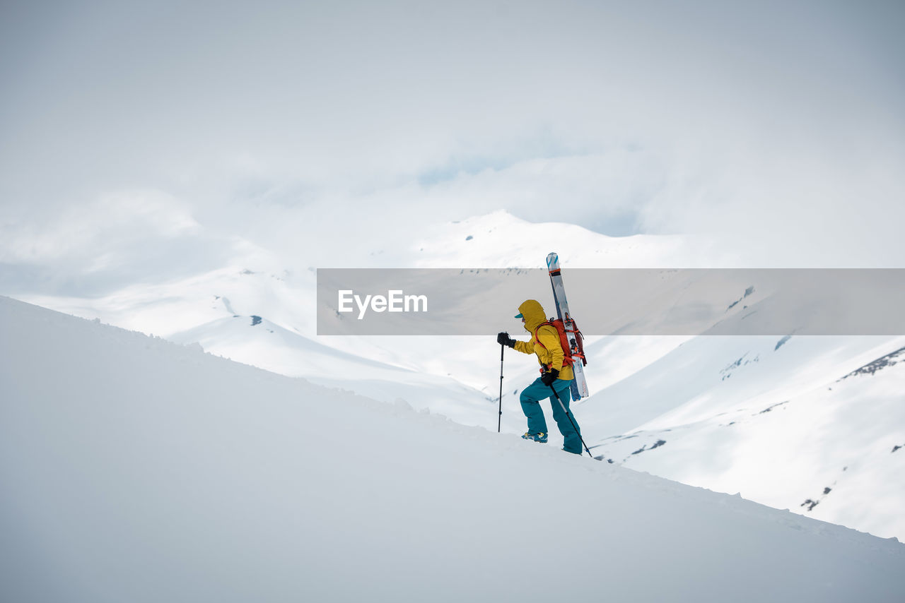 A person walks up a mountain ridge with skis on her back