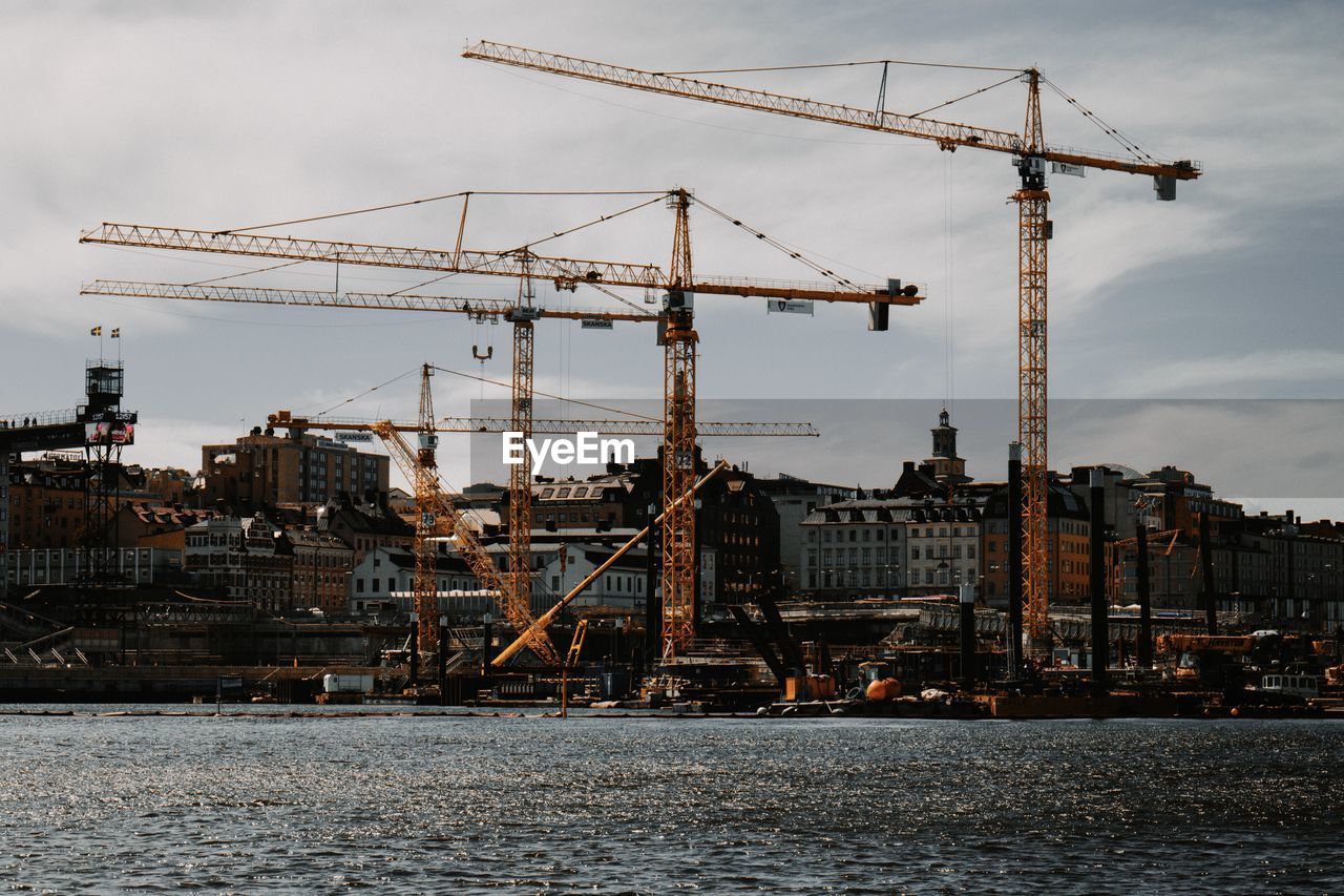 Cranes at construction site in city against sky