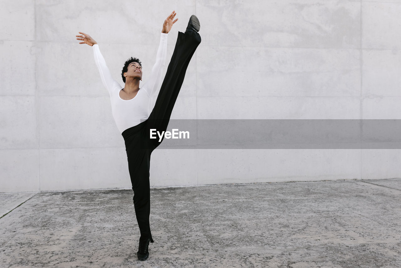 Flexible male dancer looking up while stretching leg against wall