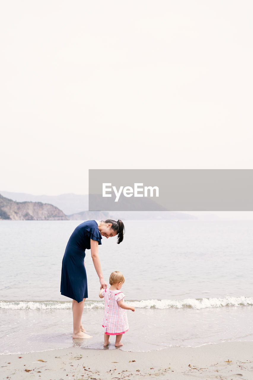 FATHER AND DAUGHTER ON BEACH AGAINST SKY