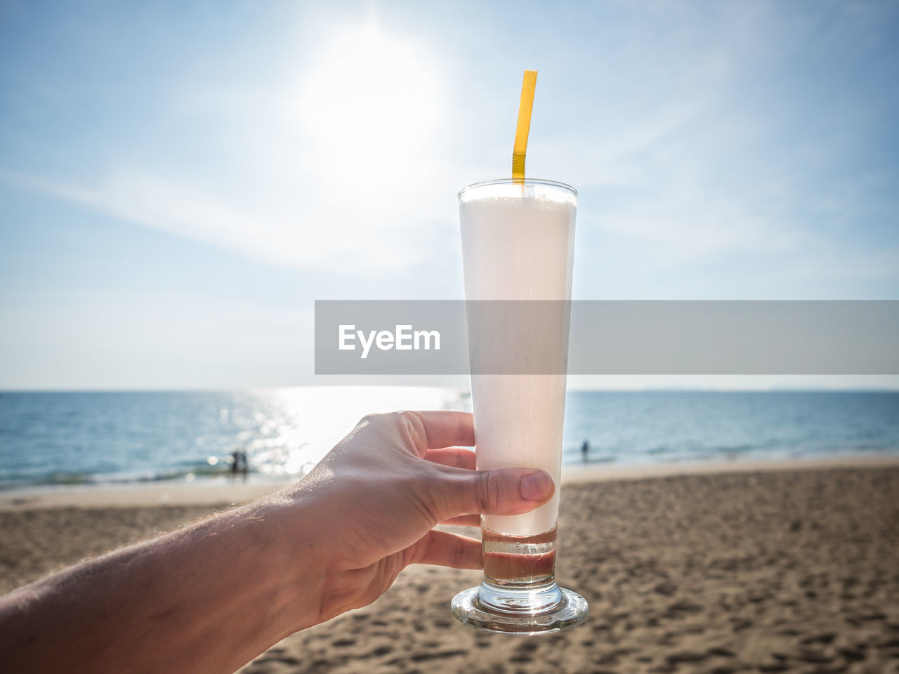 Close-up of hand holding drink at beach against sky