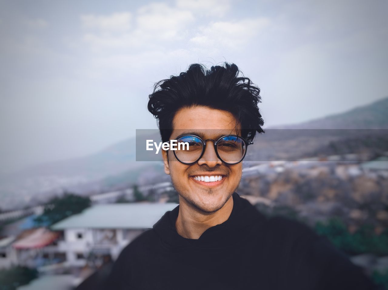 Portrait of smiling young man against cityscape and sky