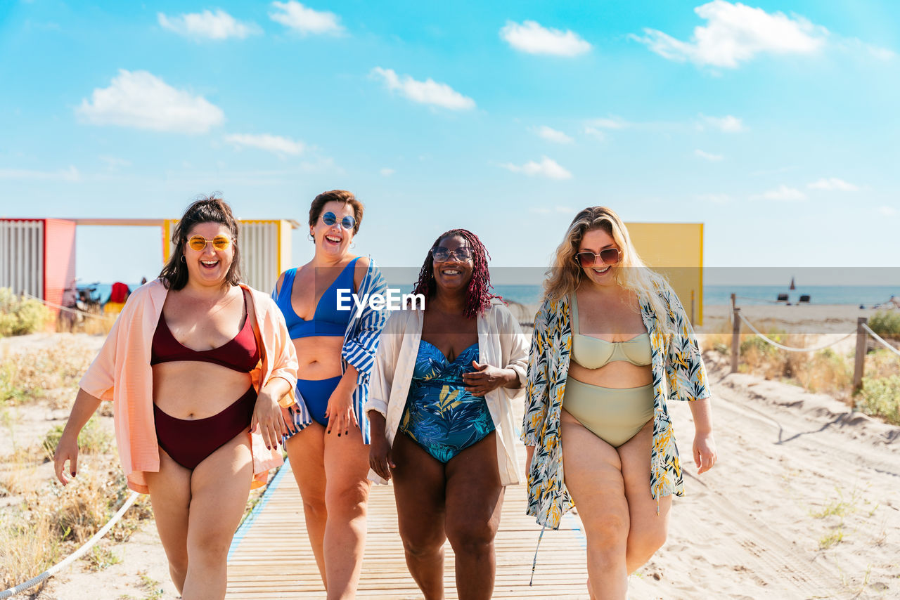 smiling friends in bikini standing at beach